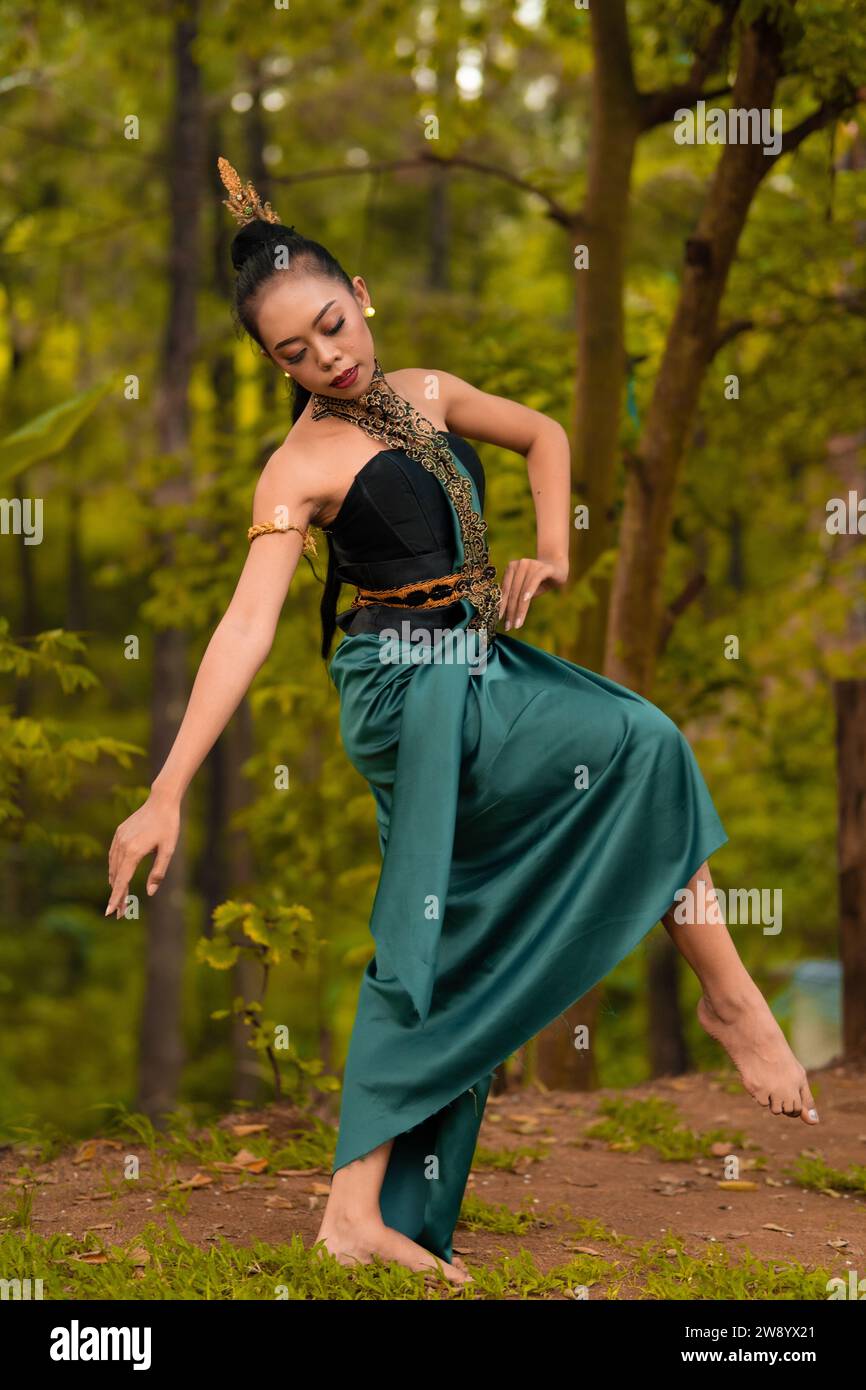 Indonesian woman dancing in the forest while wearing a traditional green costume during the festival inside the village Stock Photo