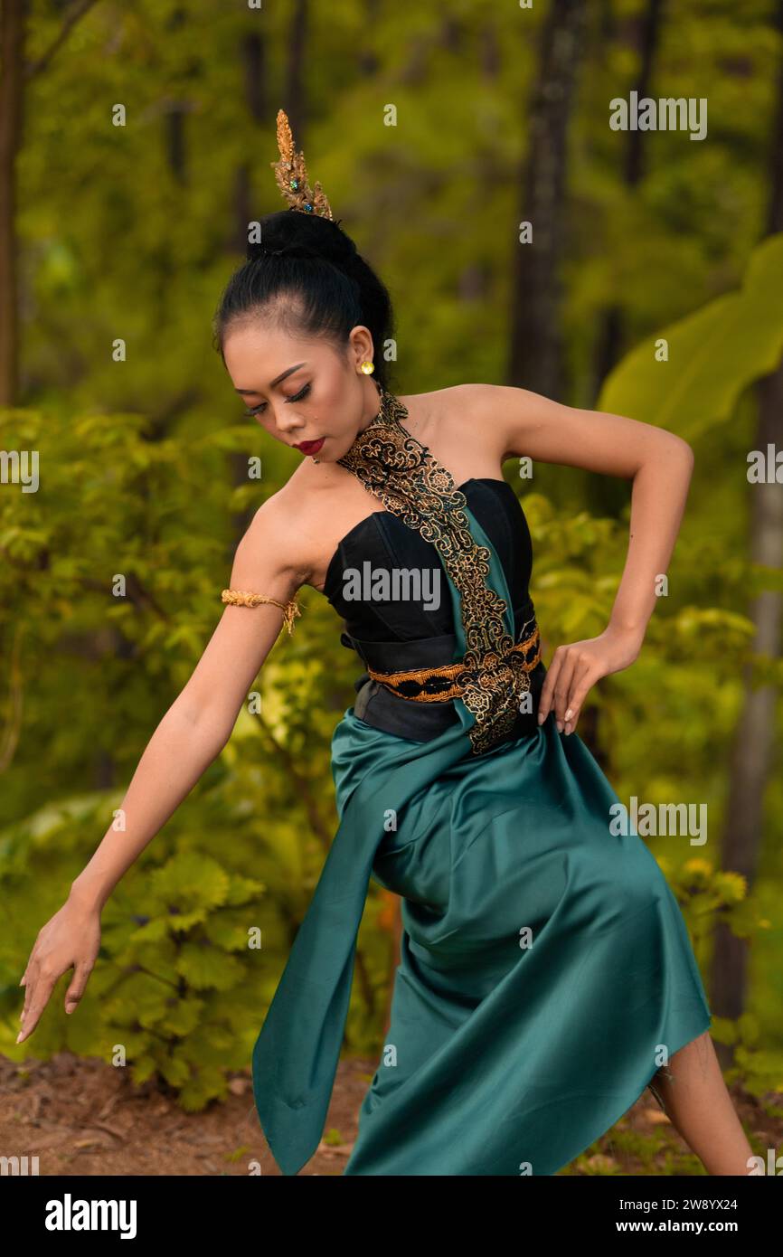 Indonesian woman dancing in the forest while wearing a traditional green costume during the festival inside the village Stock Photo