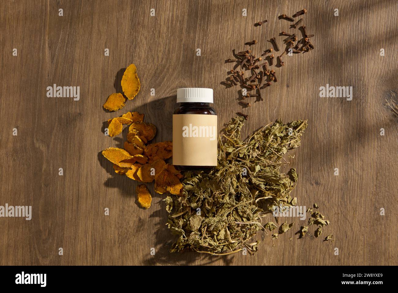Top view of an amber bottle unlabeled displayed on wooden table background with traditional medicines. Turmeric, mint and cloves are all folk medicine Stock Photo