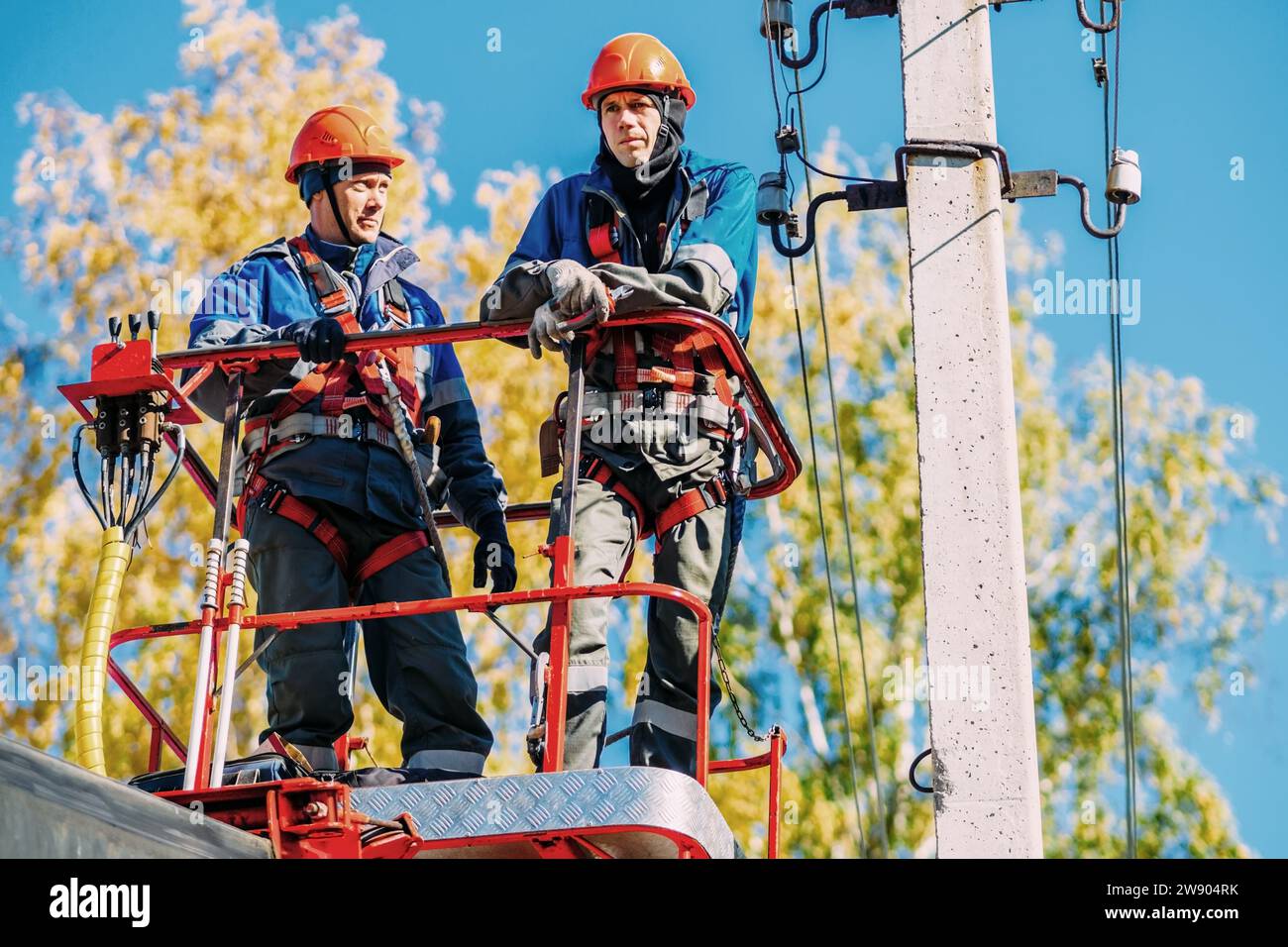 Two professional electricians in hard hats are repairing power lines