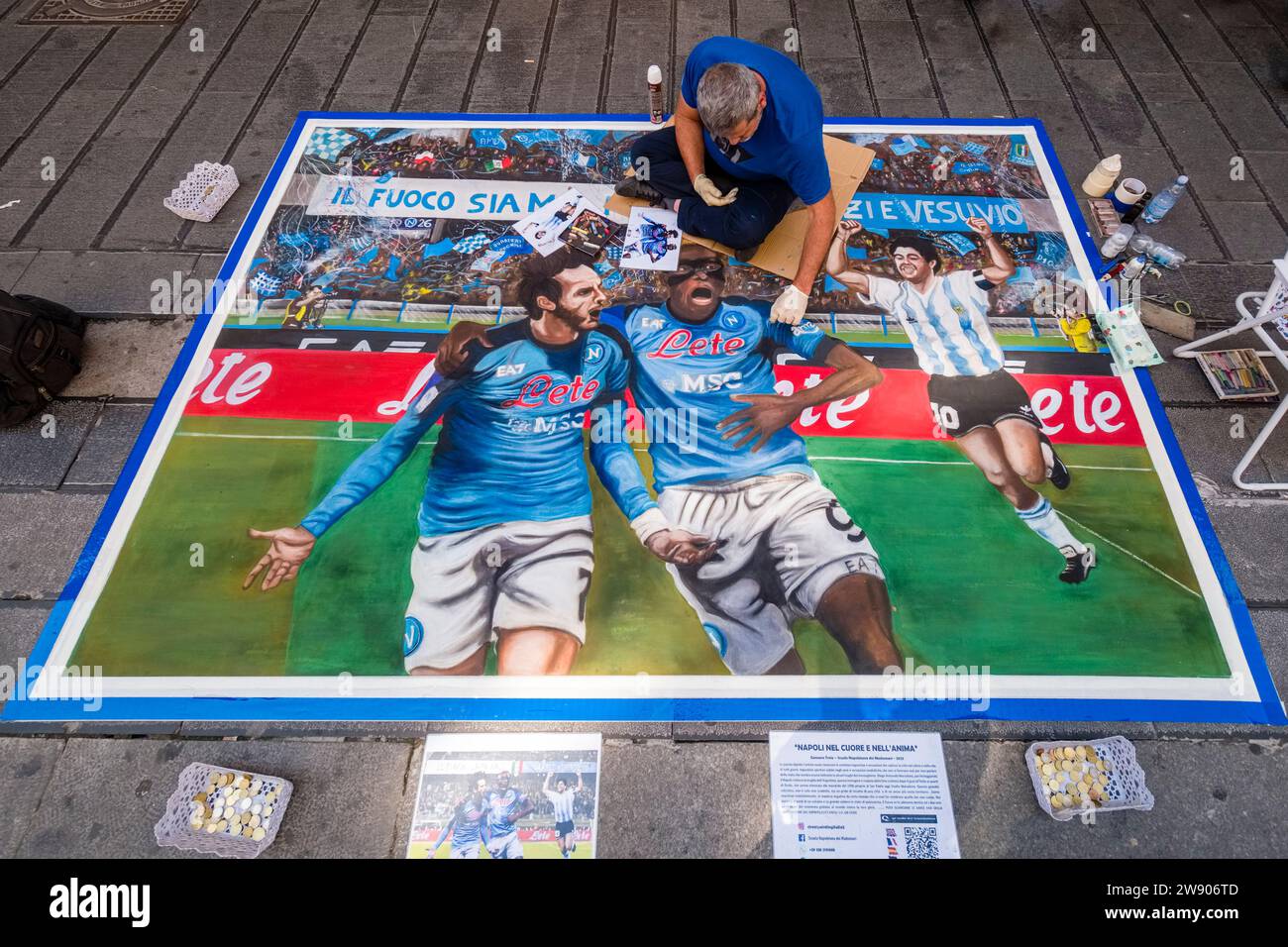 An artist uses chalk to draw a large picture of footballers from SSC Napoli, who have just won the Italian championship in 2023, on the street. Stock Photo