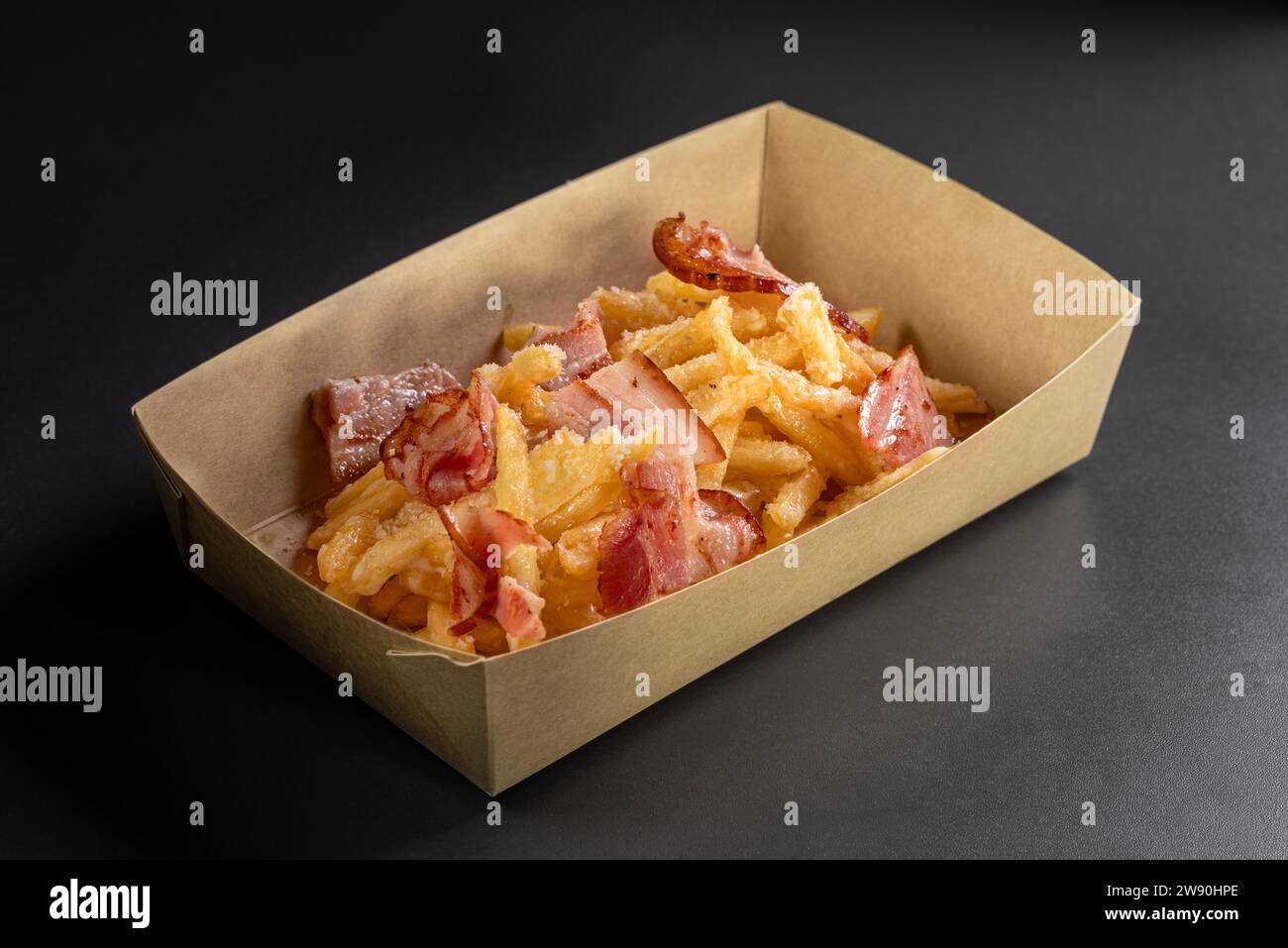 Fondue fried potatoes with cheese and crispy bacon on a black background, in a container for