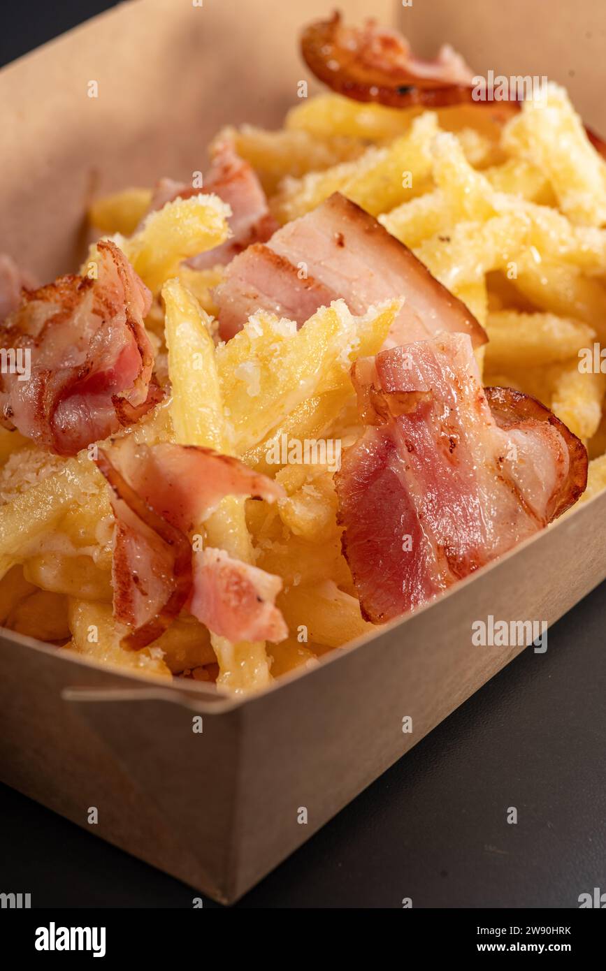 Fondue fried potatoes with cheese and crispy bacon on a black background, in a container for