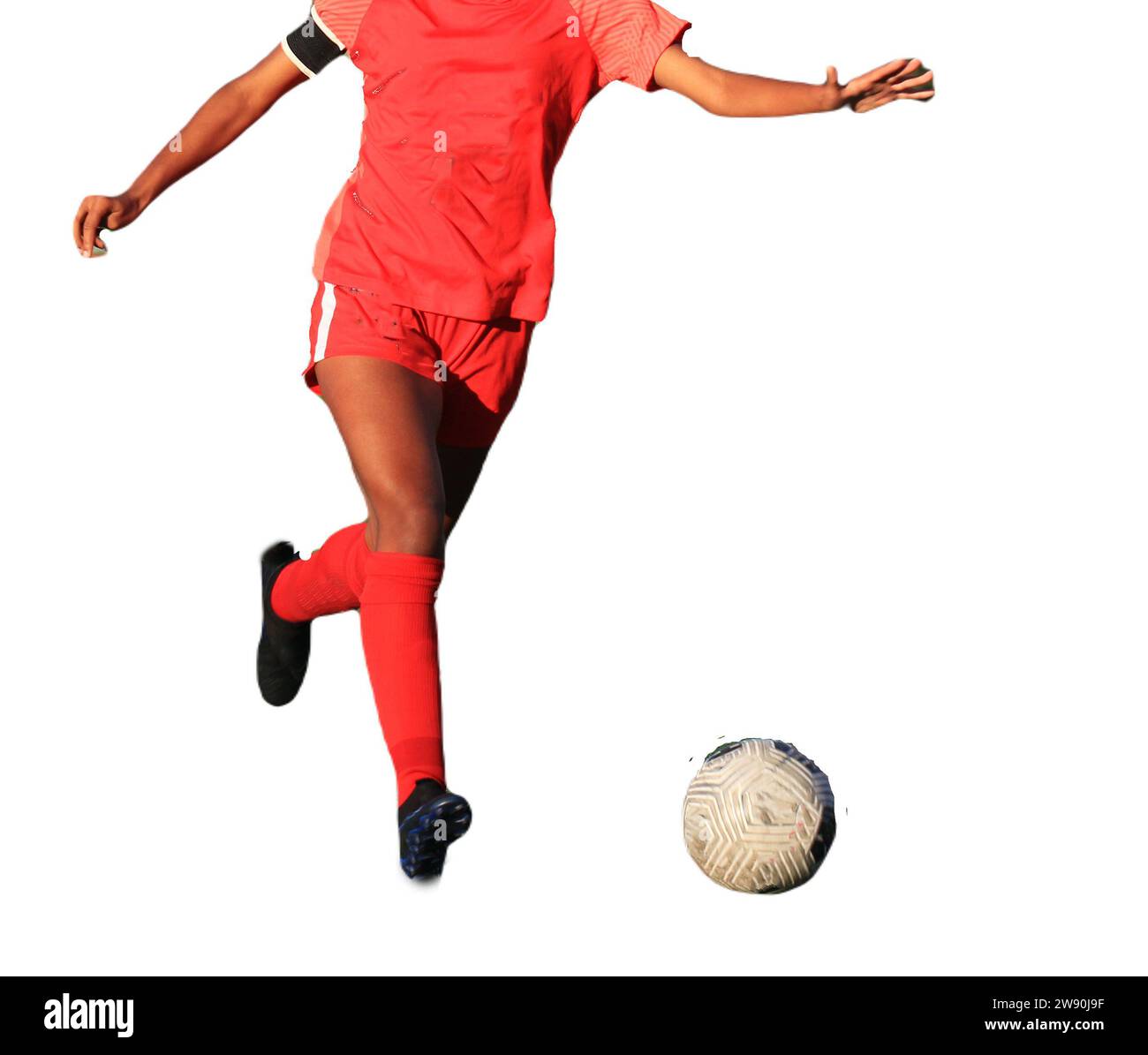 A female soccer player wearing a red uniform is running with the ball with a white background. Stock Photo