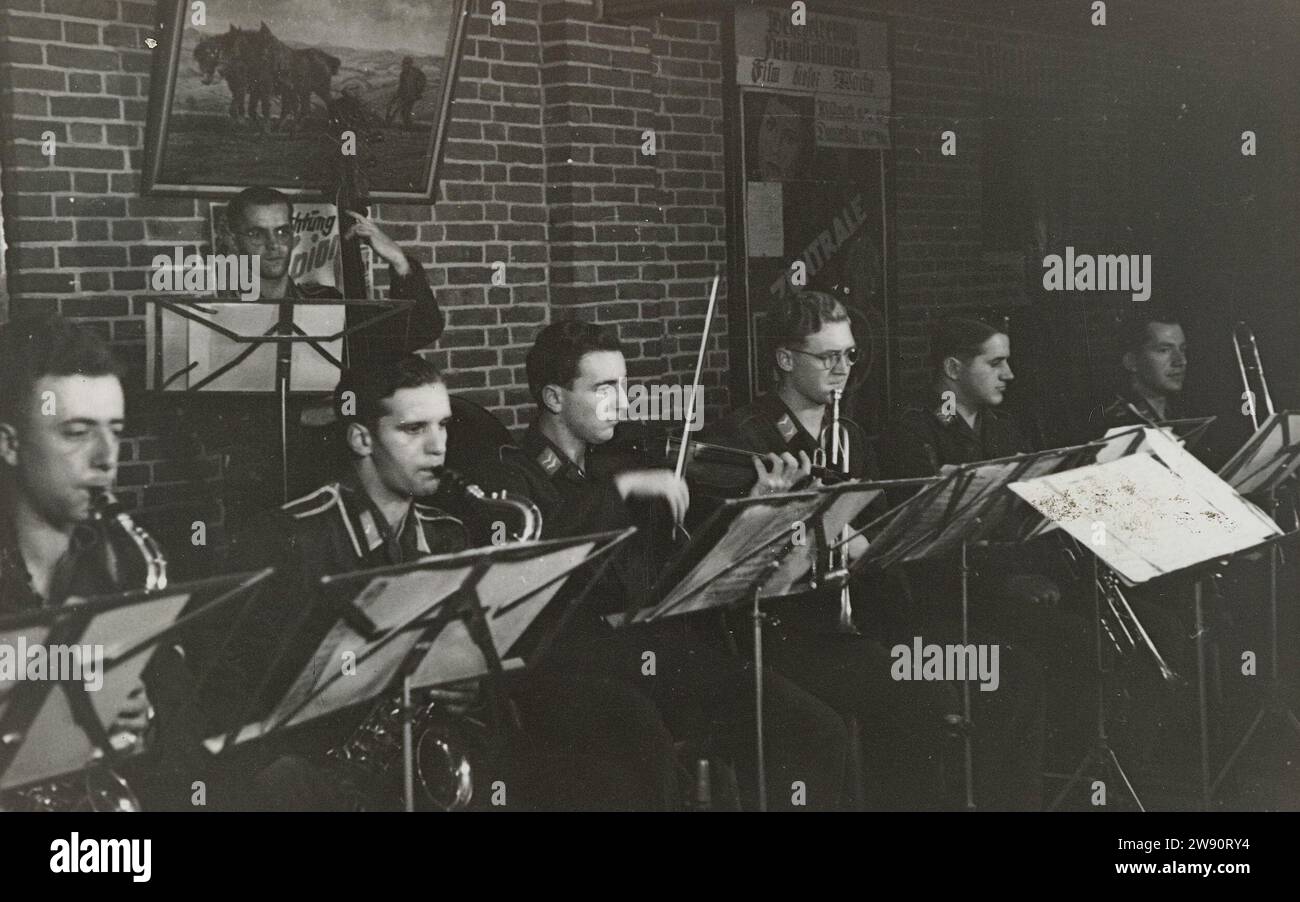 Orchestra of the Luftwaffe, 1941 - 1942 photograph Luftwaffe soldiers play music, on bladder and string instruments. For them a standard with music. On the wall a record of a plowing farmer and a film poster. Netherlands photographic support gelatin silver print occupation  war. military band Netherlands Stock Photo