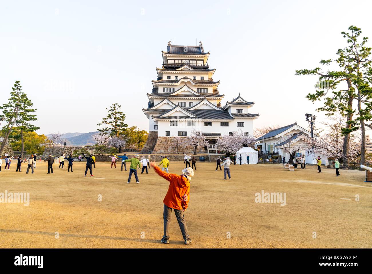 Fukuyama castle, Japan. Old people taking part in a group exercise session in front of the newly restored white borogata style keep just after sunrise Stock Photo