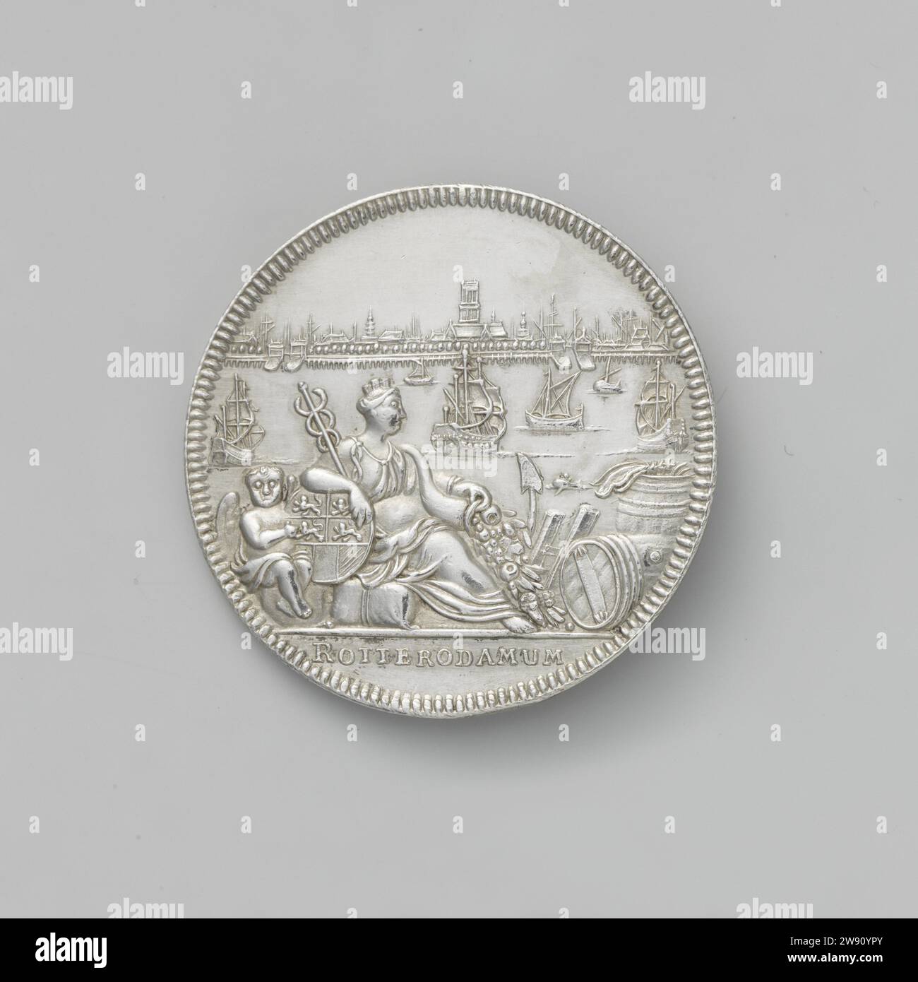 Midwifery of the city of Rotterdam, Van de Vou, 1714  Silver medal. Front: View of the city of Rotterdam aan Maas, on which six ships sail; In the foreground: crowned woman with mercury staff and horn of abundance, sitting in the midst of barrels, anchor, ladder and suit; Behind her: Angel with coat of arms; Cut: Inscription. Reverside: under the sea landscape, lit by sun: crossed trumpet and mercury staff under Hermeskop between two filled horns of abundance; Cut: Inscription. Amsterdam silver (metal) striking (metalworking)  Rotterdam Stock Photo