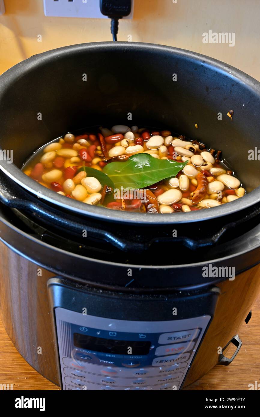 Mix of dried beans with spices soaking in water in pressure cooker pot before cooking, inexpensive meal Stock Photo
