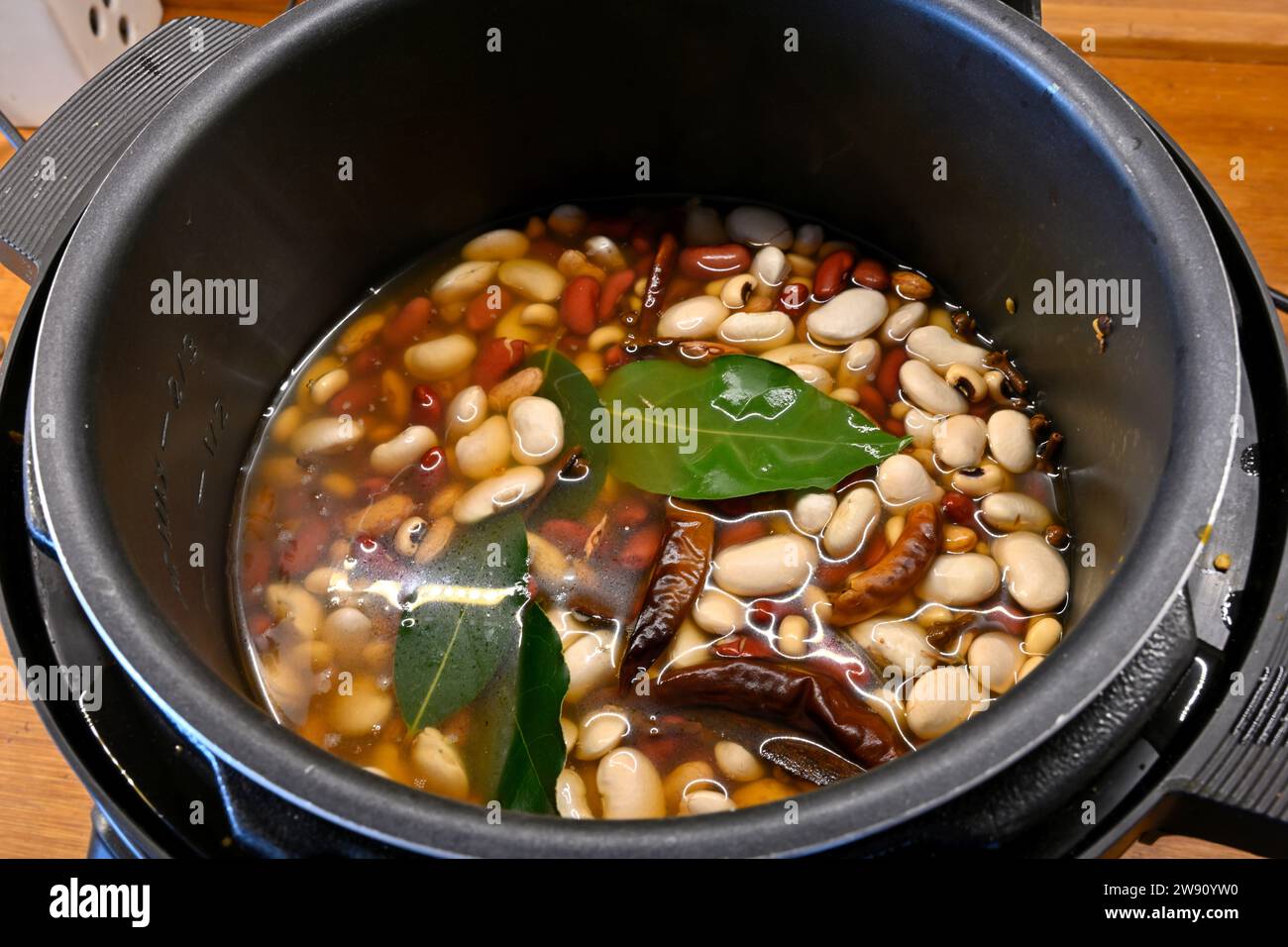Mix of dried beans with spices soaking in water in pressure cooker pot before cooking, inexpensive meal Stock Photo