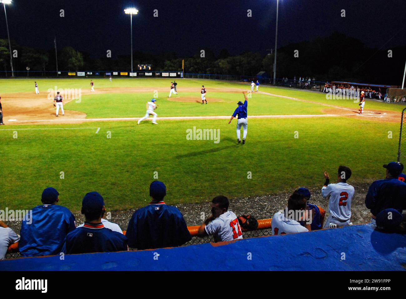 A third base coach waves a runner home during a night game in the Cape Cod Baseball League Stock Photo