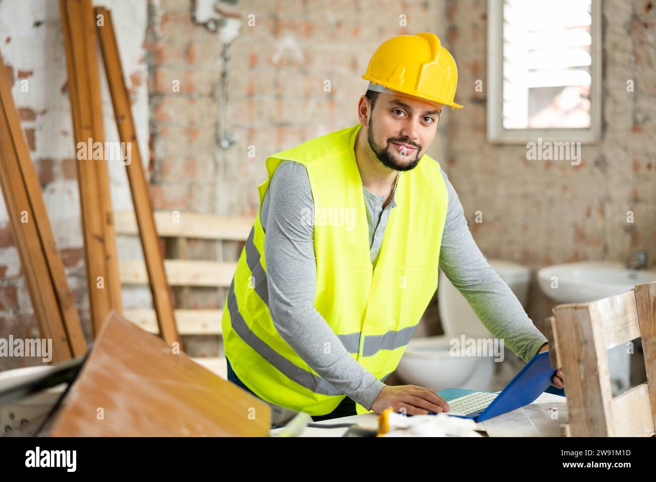 Smiling young engineer checking house renovation plan on laptop Stock Photo