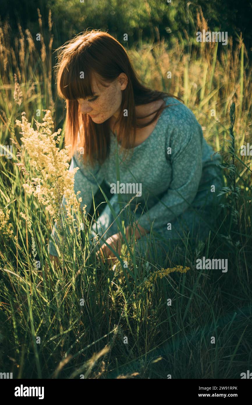 Young redhead woman kneeling in meadow Stock Photo