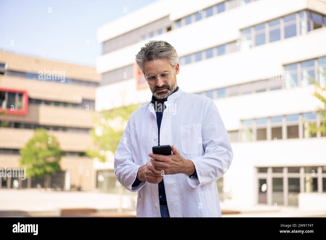 Doctor using mobile phone in front of buildings Stock Photo