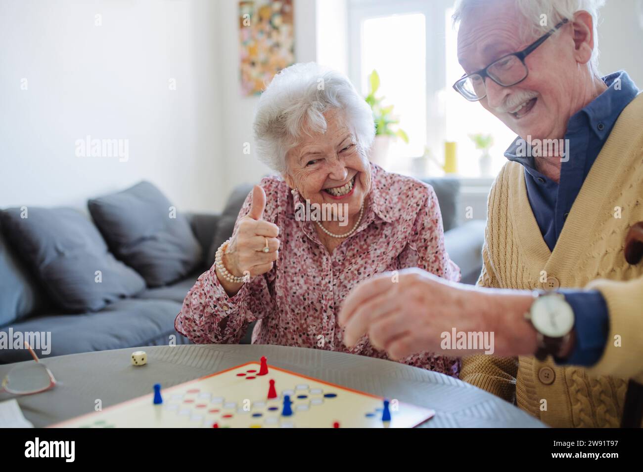 Cheerful woman gesturing thumbs up and playing ludo with man at table Stock Photo