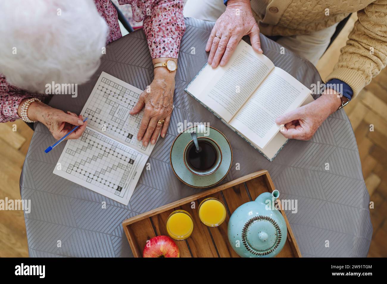 Senior man reading book with woman doing crossword puzzle at table Senior man reading book with woman doing crossword puzzle at table