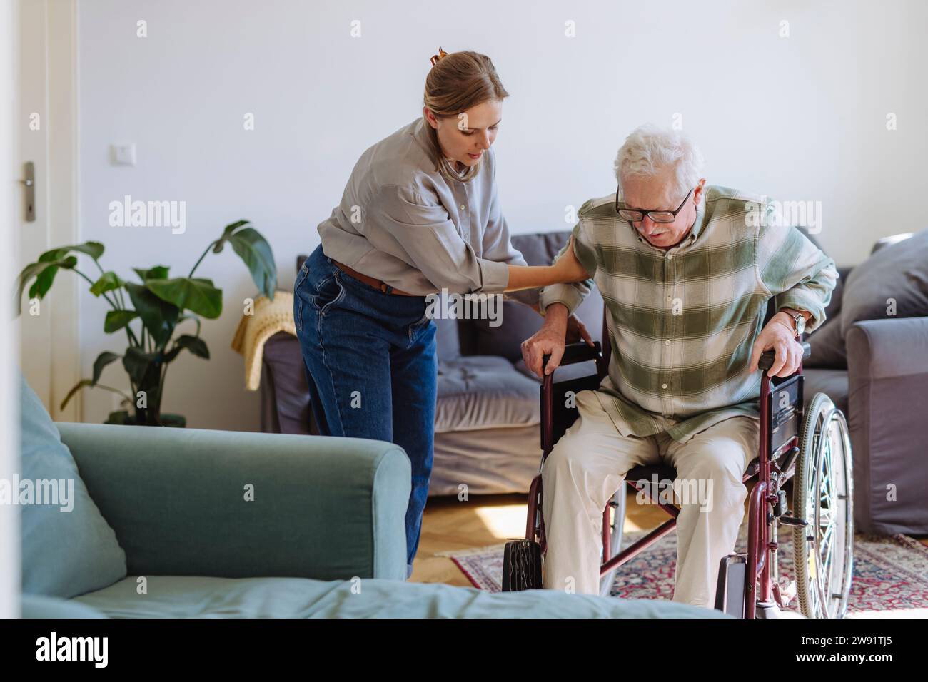 Healthcare worker helping senior man sitting in wheelchair at home Stock Photo
