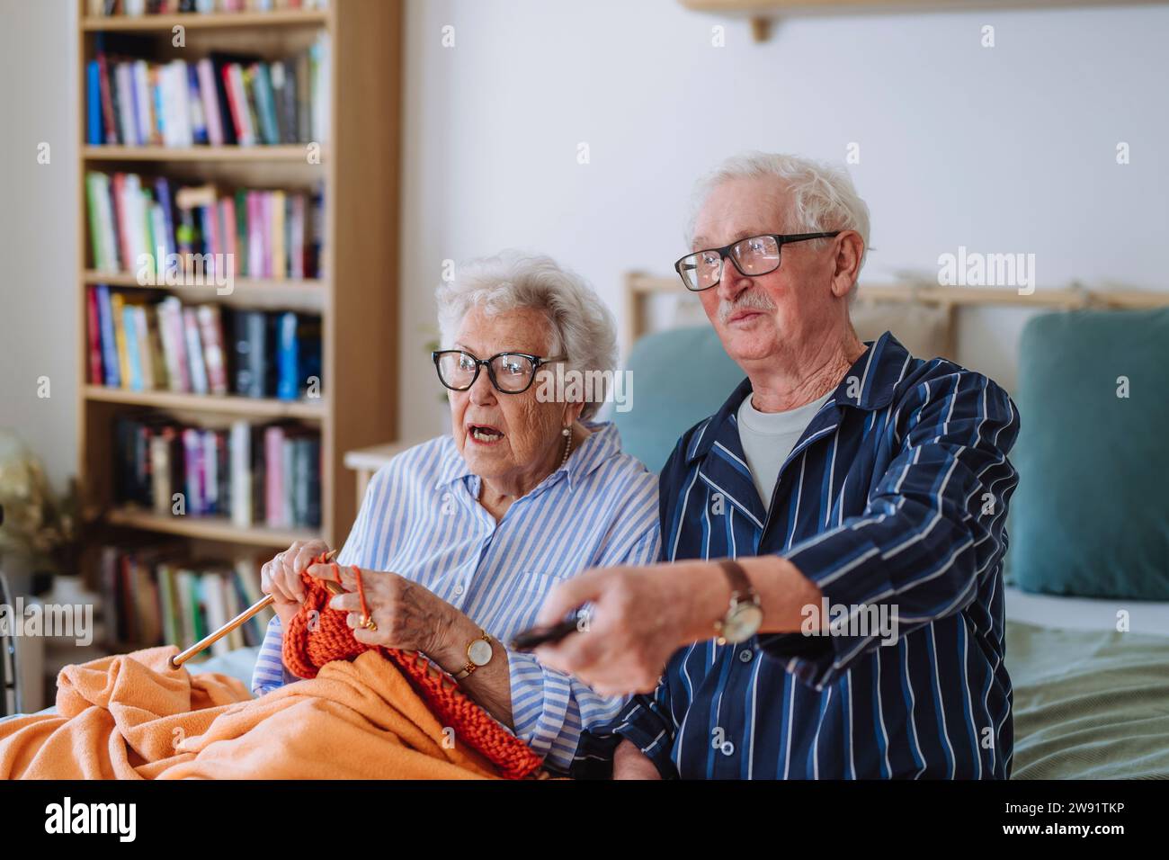 Senior woman knitting with man holding remote and watching TV at home Stock Photo