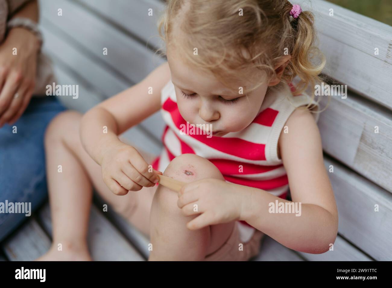 Little girl blowing on injured knee and putting on band aid Stock Photo