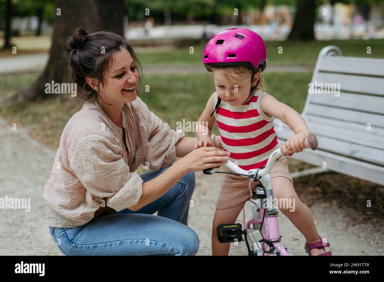 Mother putting safety helmet on little girl's head learning to ride a bike in the city park Stock Photo