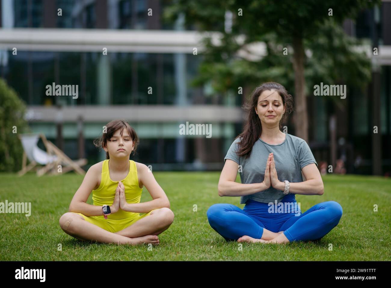 Mother and daughter spending together time outdoors practicing yoga in the city park Stock Photo