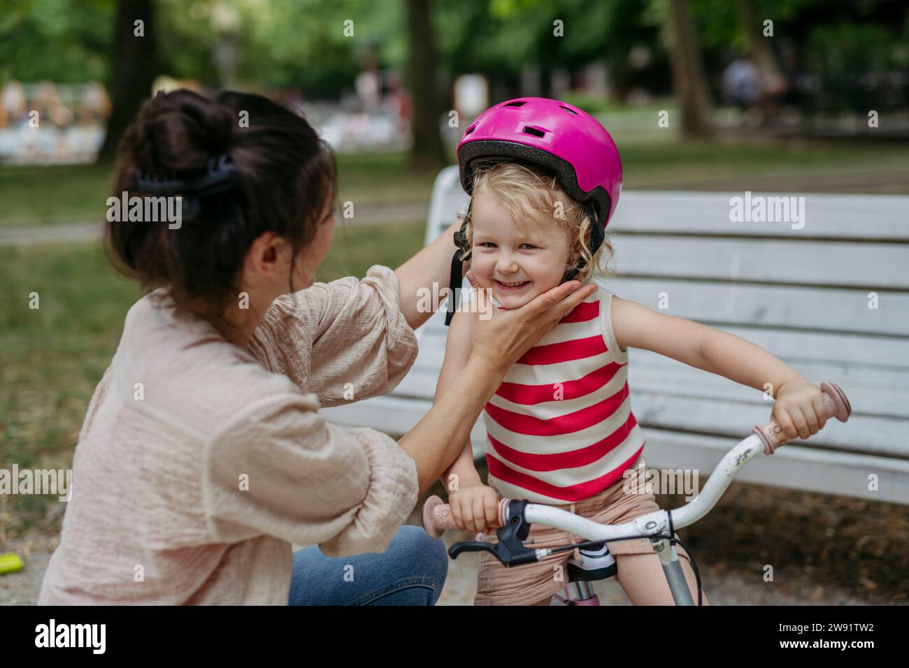 Mother putting safety helmet on little girl's head learning to ride a bike in the city park Stock Photo