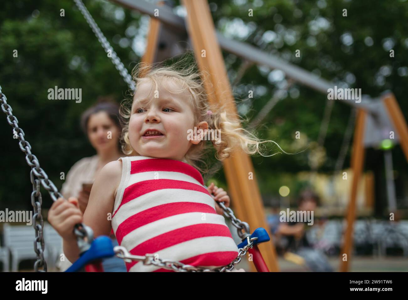 Little toddler girl and mother have fun at playground swinging on a swing Stock Photo