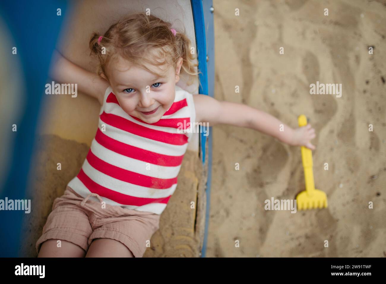 Happy little girl with toy rake lying in climbing frame at the ...