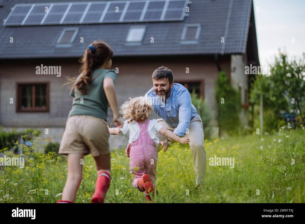 Father and daughters having fun in front their family house with solar panels on the roof Stock Photo