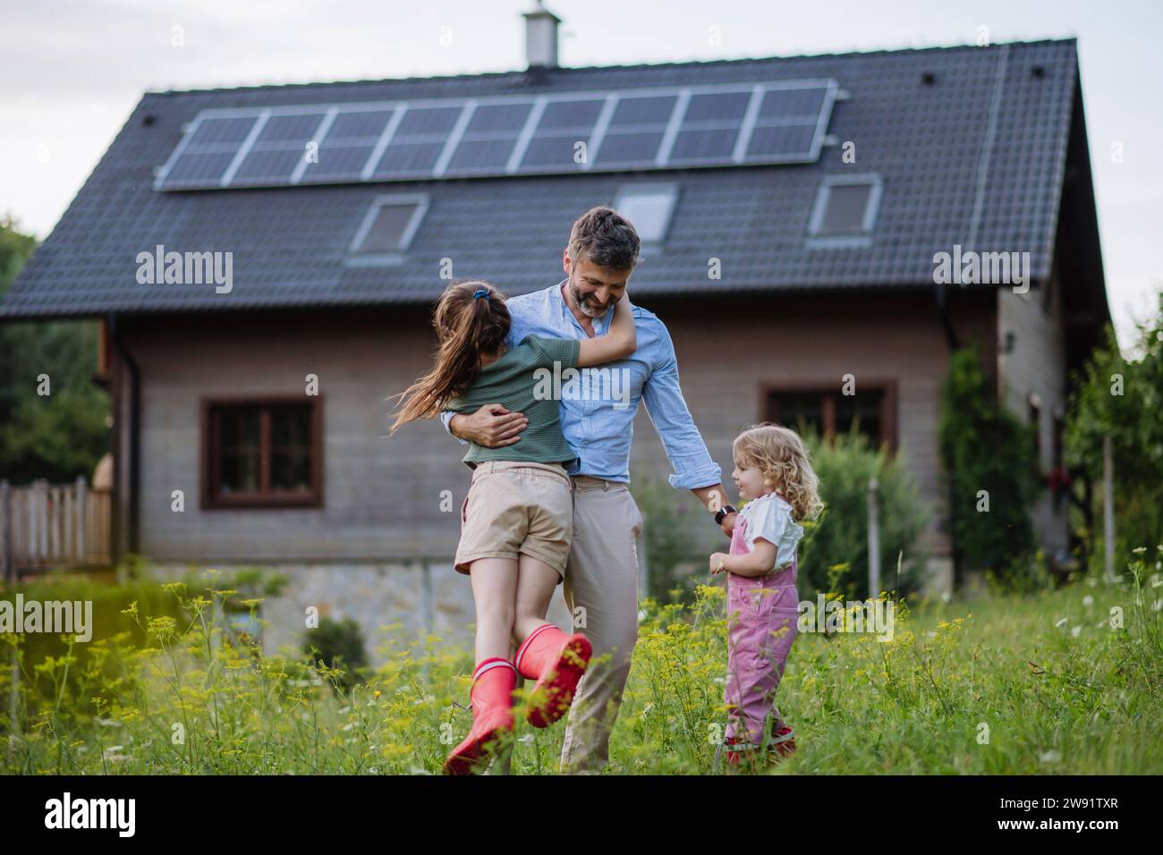 Father and daughters having fun in front their family house with solar panels on the roof Stock Photo
