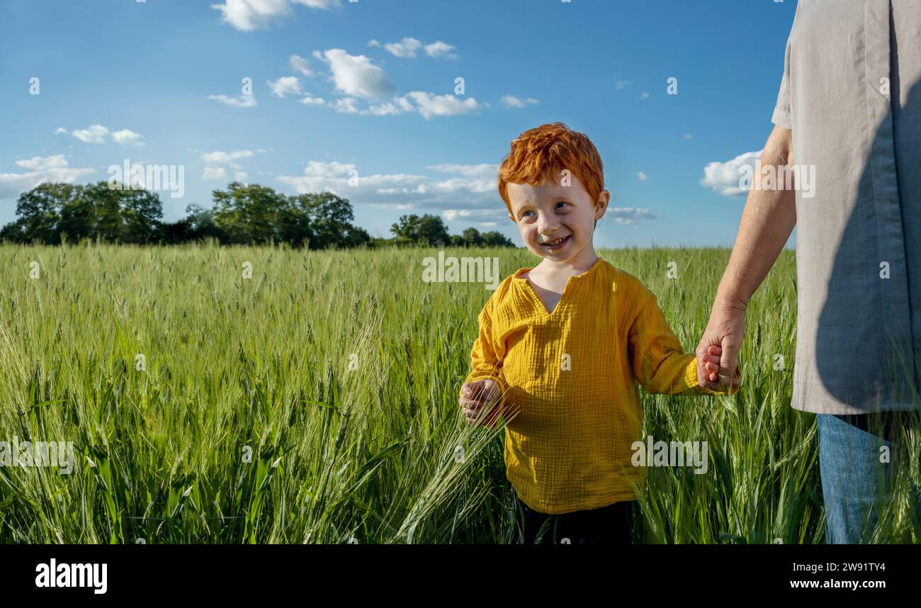 Smiling boy holding hand of grandmother walking in field Stock Photo