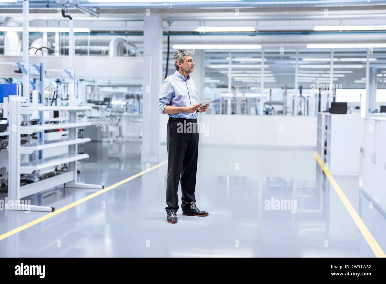 Thoughtful engineer with tablet PC standing at factory Stock Photo