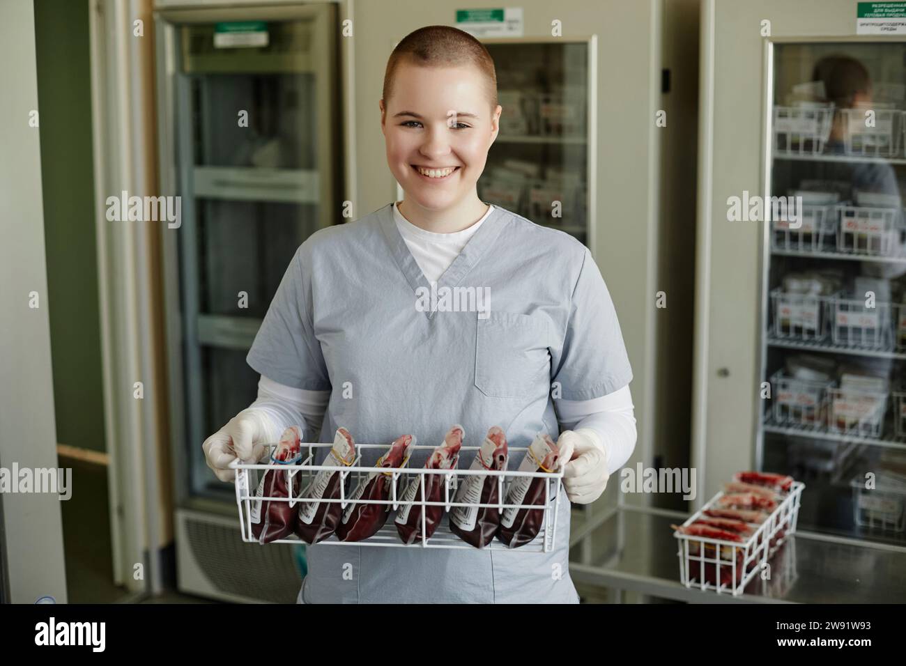 Smiling lab technician holding rack of blood bags at clinic Stock Photo
