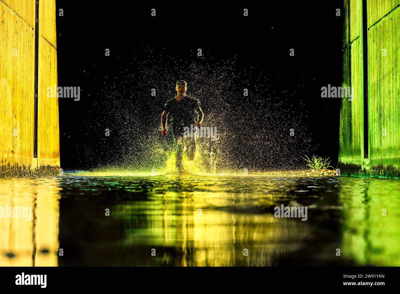 Man running in river water with neon lights under bridge Stock Photo