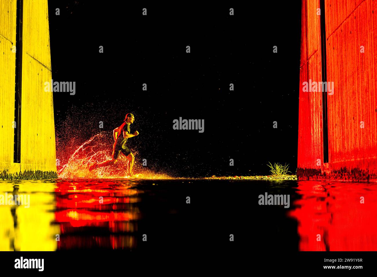 Young man running in river water with neon lights under bridge Stock Photo