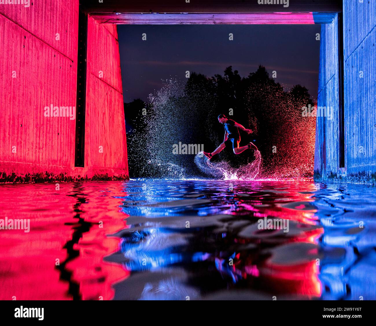 Man jumping in river water under bridge with neon lights at night Stock Photo