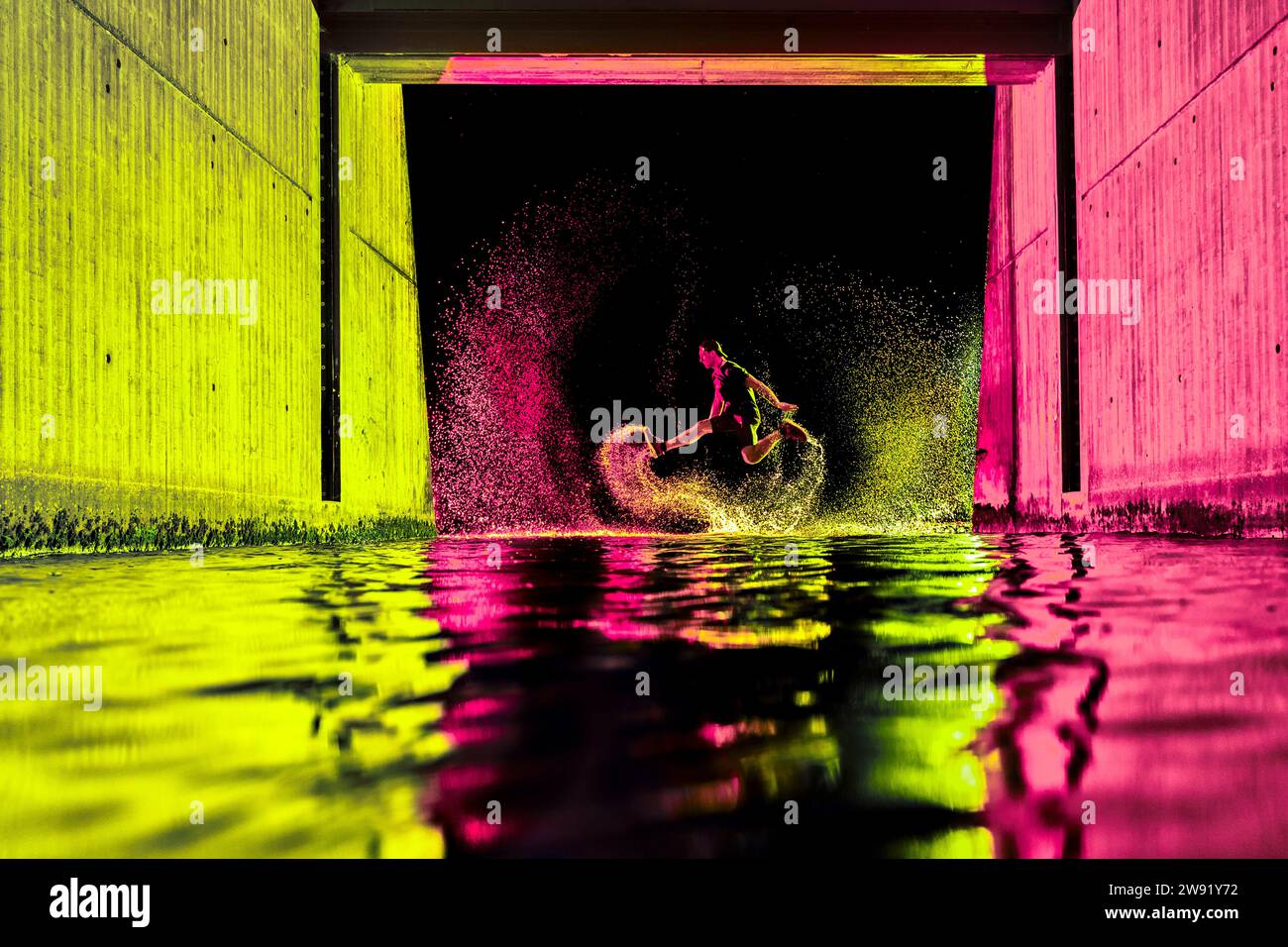 Young man jumping in river water with neon lights under bridge at night Stock Photo