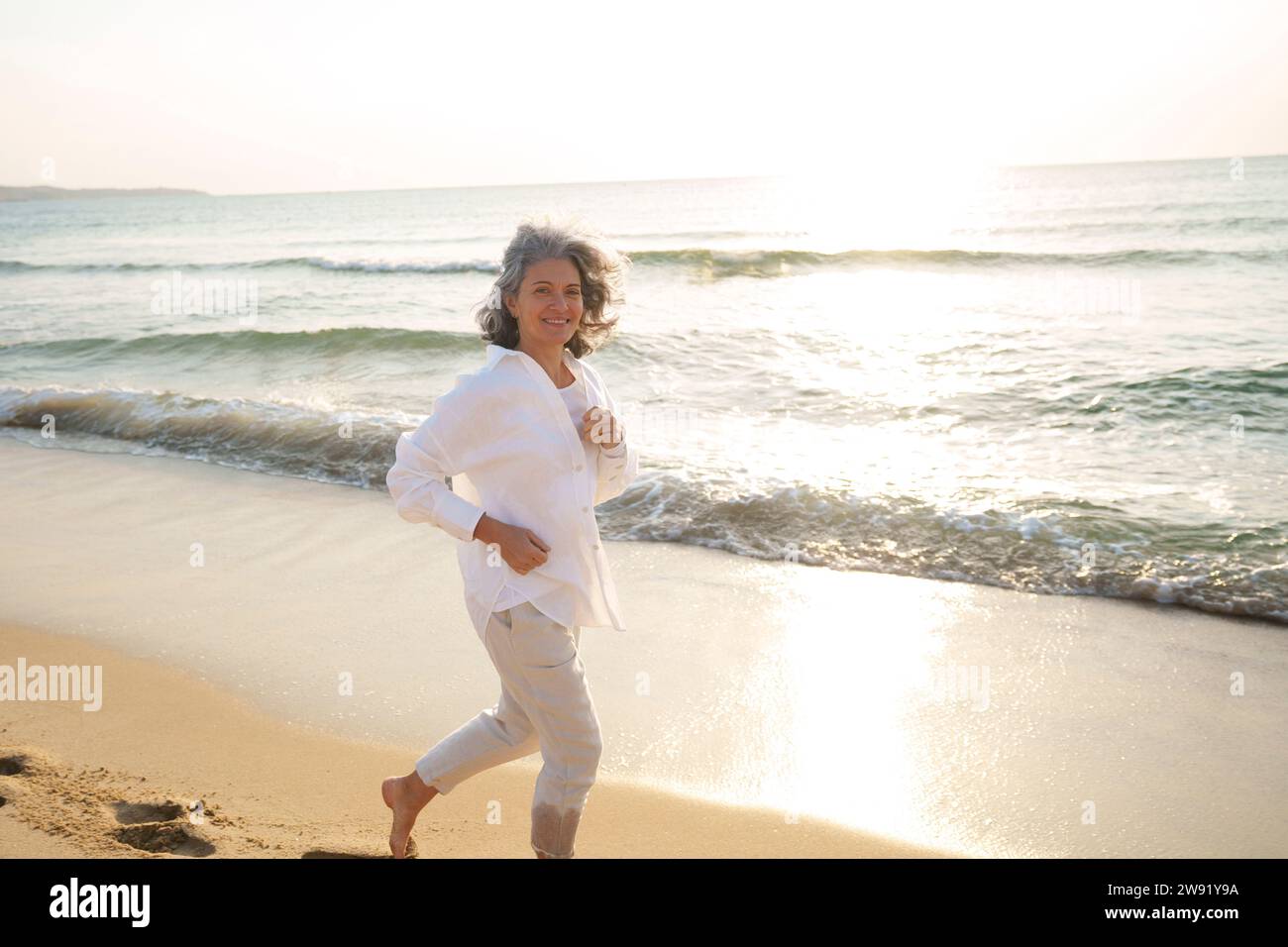 Smiling mature woman running at beach Stock Photo