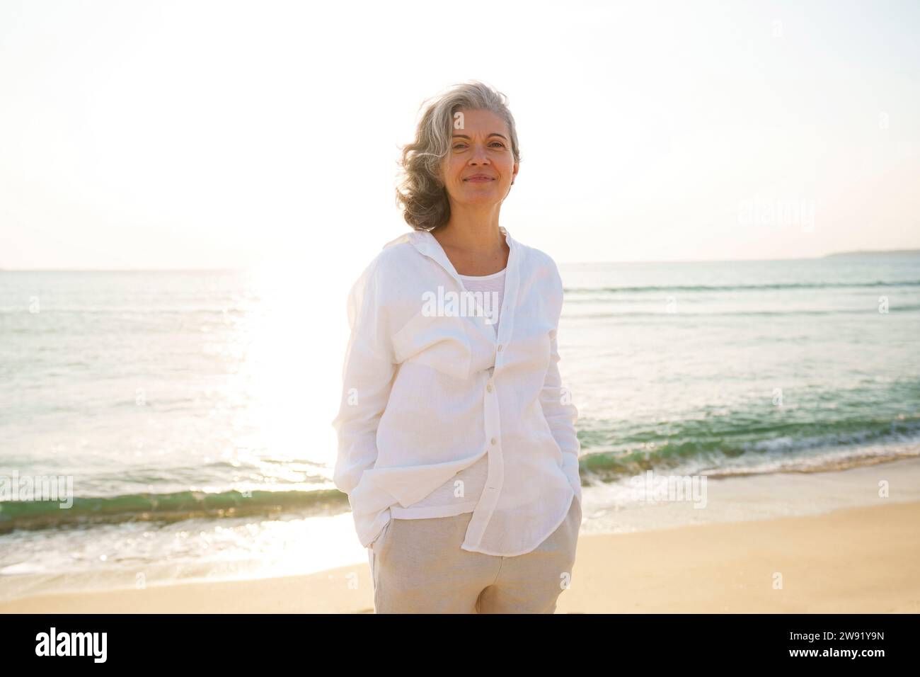 Smiling mature woman standing in front of sea at beach on sunny day ...