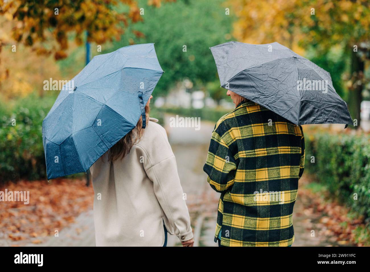 Mother and daughter holding umbrellas and walking in autumn park Stock Photo