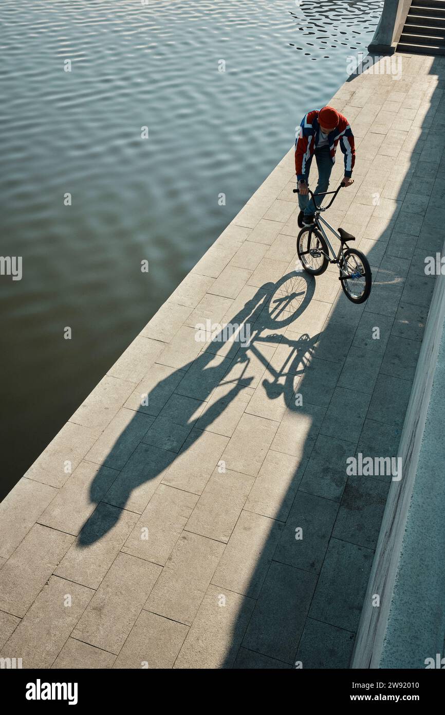 Man doing stunt with BMX bike on embankment near lake Stock Photo