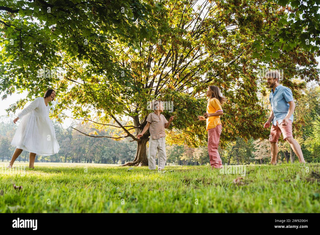 Father and mother having fun with children near tree at park Stock Photo