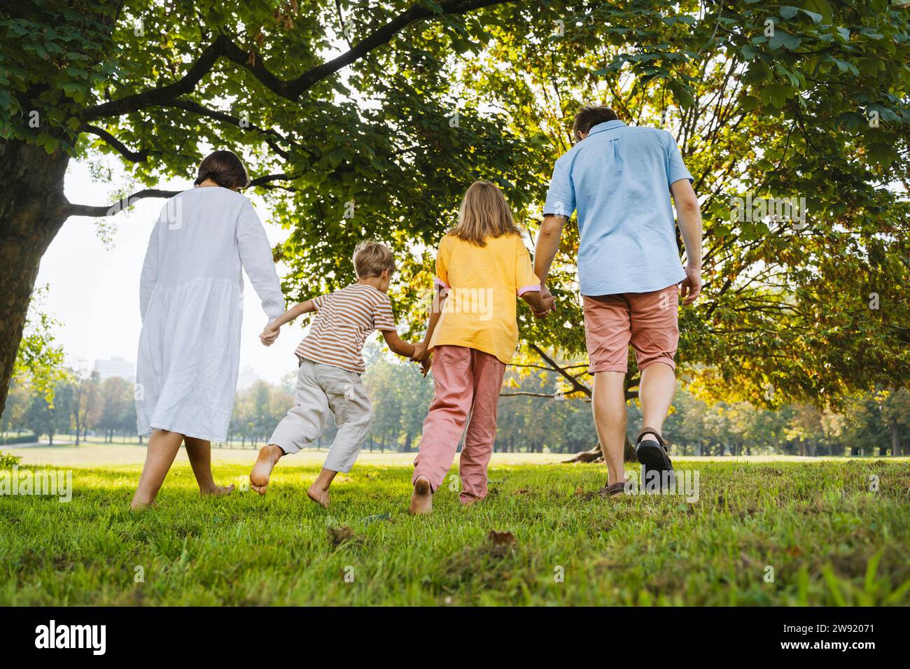 Family holding hands and walking on grass at park Stock Photo