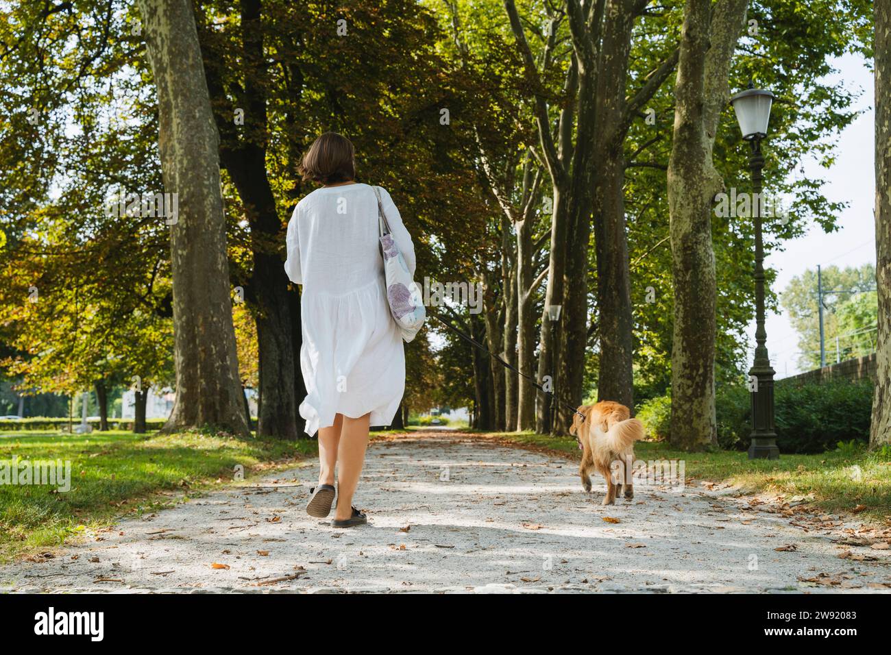 Woman walking with dog on footpath at park Stock Photo