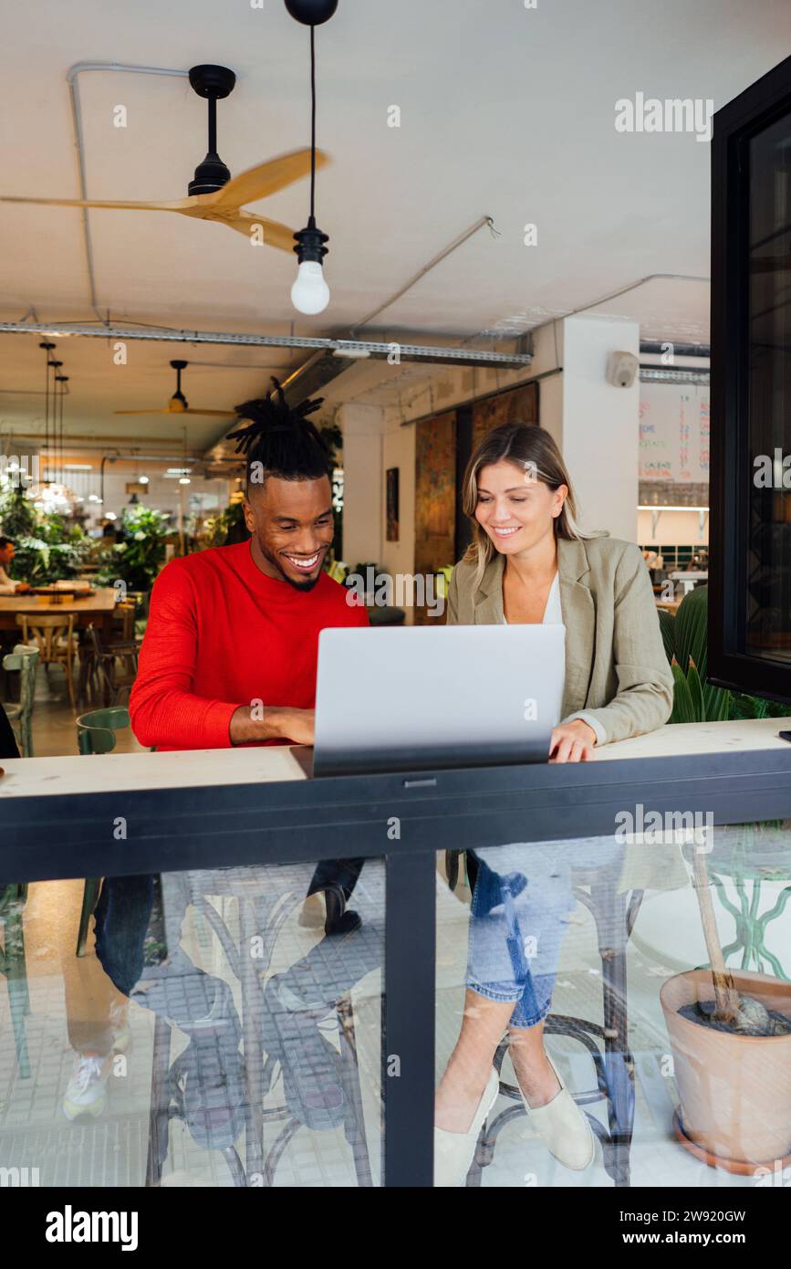 Smiling business colleagues working on laptop at cafe Stock Photo