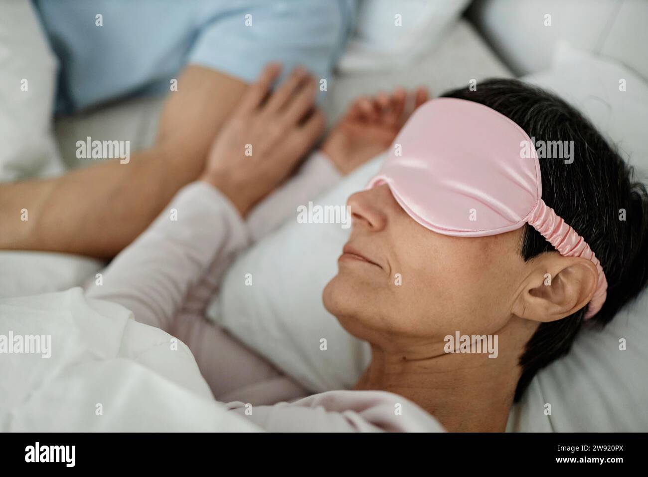 Woman wearing sleeping mask while lying in bed next to her husband
