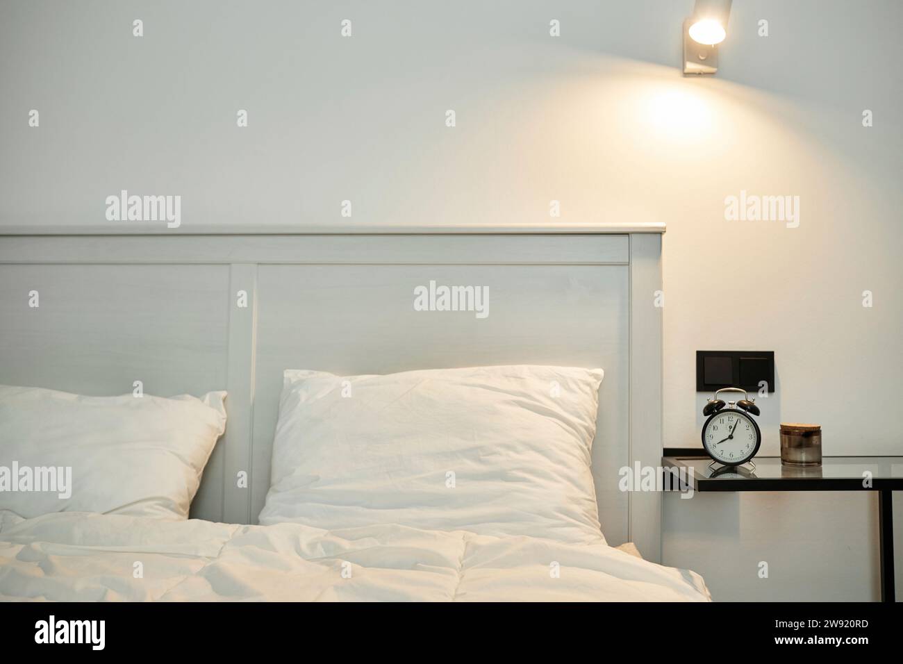 Bedroom interior, bed with white linen and bedside table with alarm clock on it Stock Photo