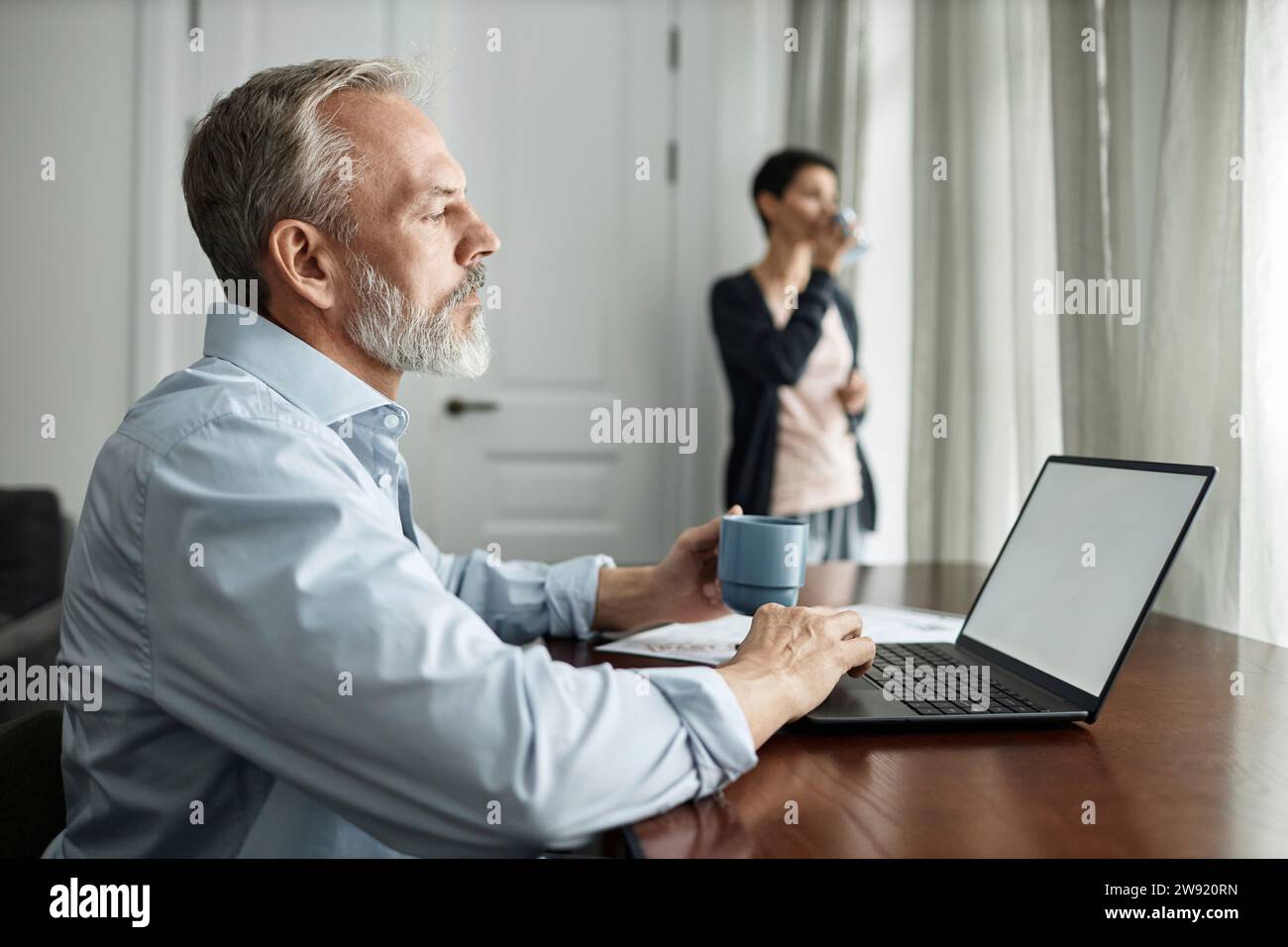 Man using laptop and drinking tea while spending time at home with wife Stock Photo