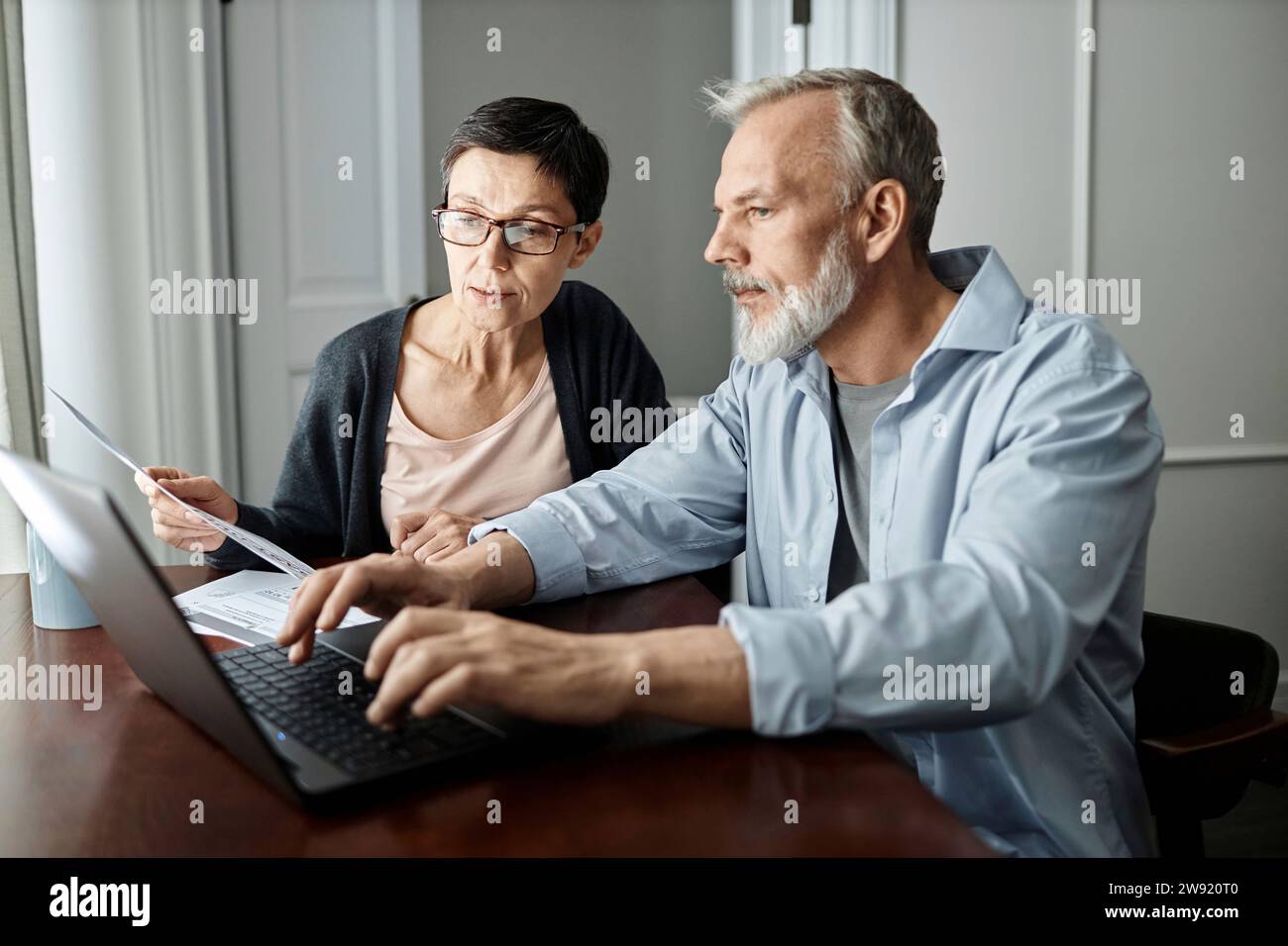 Senior couple talking about family business issues while sitting at table in front of laptop at home Stock Photo