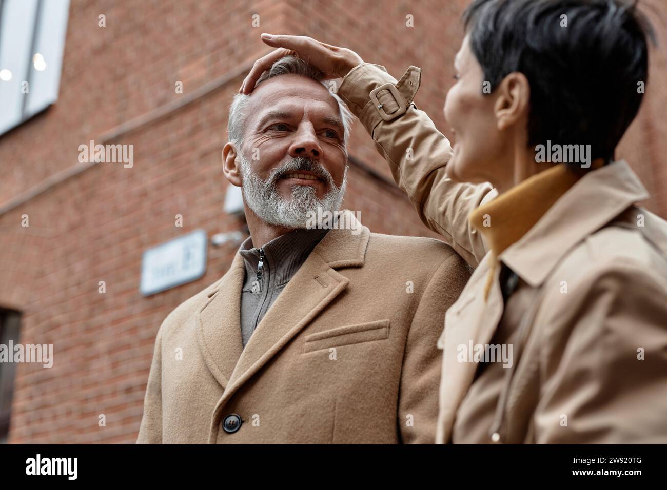 Woman fixing her husbands hair while walking at street Stock Photo