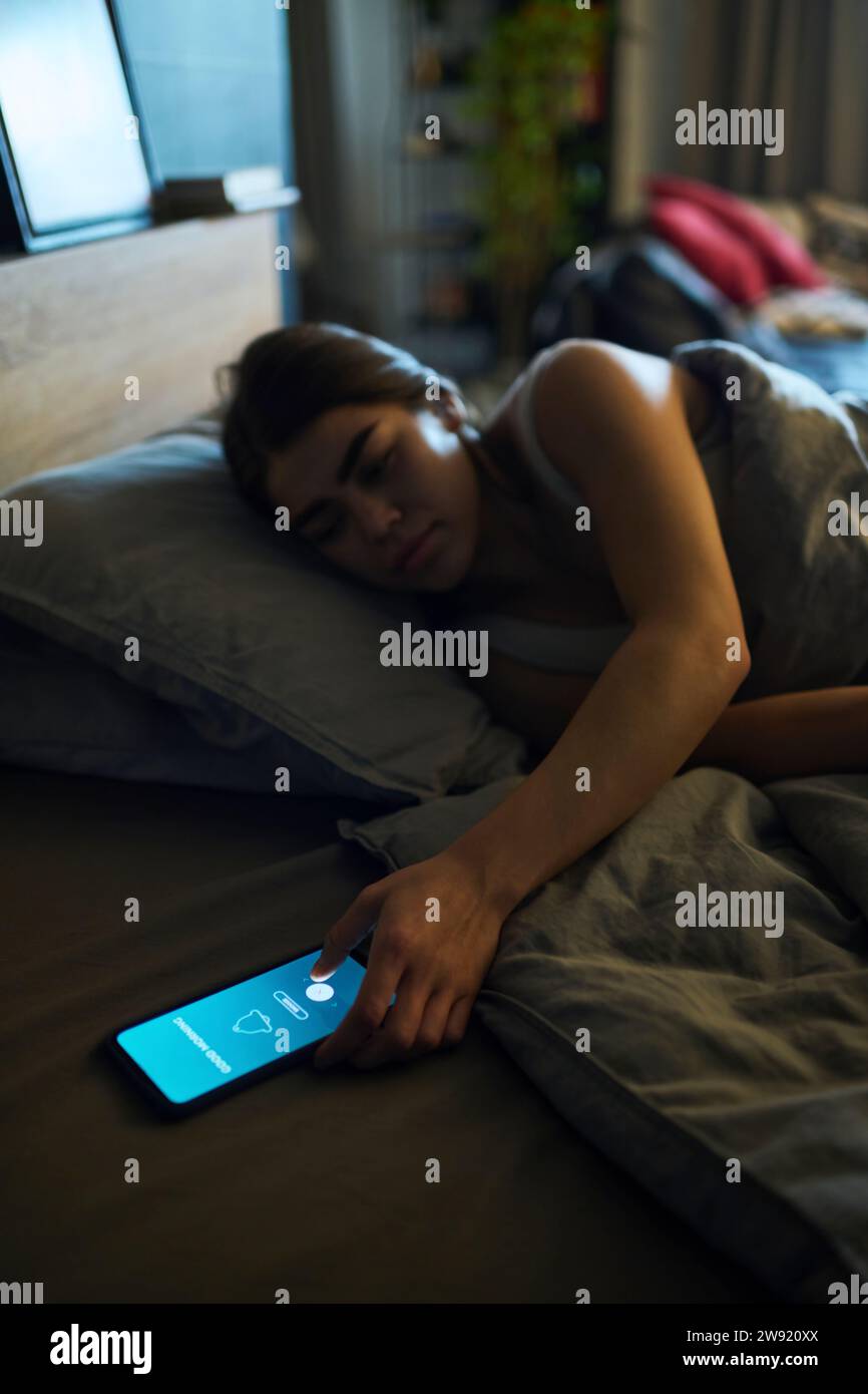 Young woman turning off alarm clock on smart phone at home Stock Photo